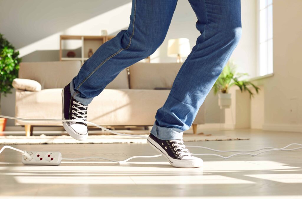 Person tripping over an electrical cord at home, risk of slip and fall accident injury.