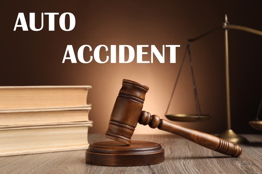Auto accident law: Judge's gavel, scales of justice, and books arranged on a wooden table against a brown background.