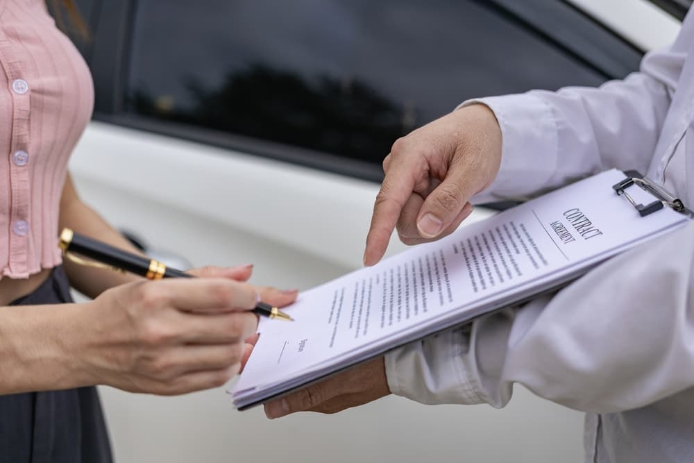 Car claim process: An insurance agent writes on a clipboard while inspecting the vehicle after an accident, as the claim is evaluated and processed.