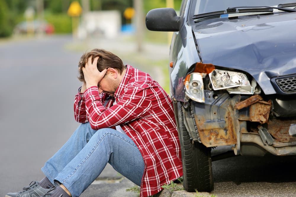 An injured man sits near his car following an accident.