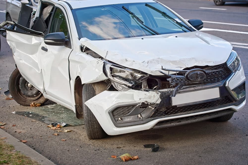 A car shows severe damage with broken headlights and crushed front and rear ends, illustrating the aftermath of a high-impact traffic accident and the destruction caused by the collision.








