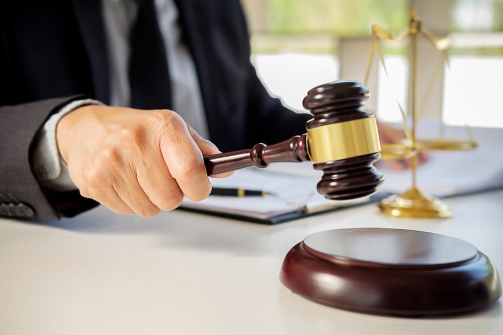 Judge’s gavel in the foreground with justice lawyers having a team meeting at a law firm in the background—symbolizing legal concepts and the practice of law.