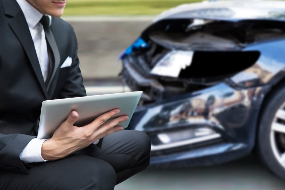 An insurance agent or investigator examines a car accident claim report on a tablet.