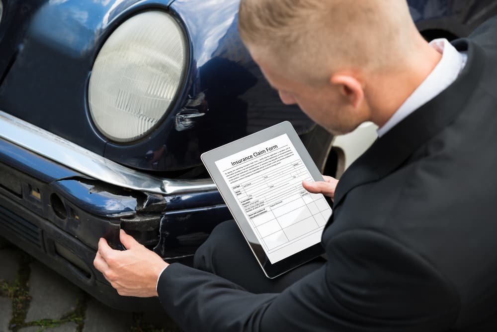 Insurance Agent Inspecting Damaged Car With Insurance Claim Form On Digital Tablet