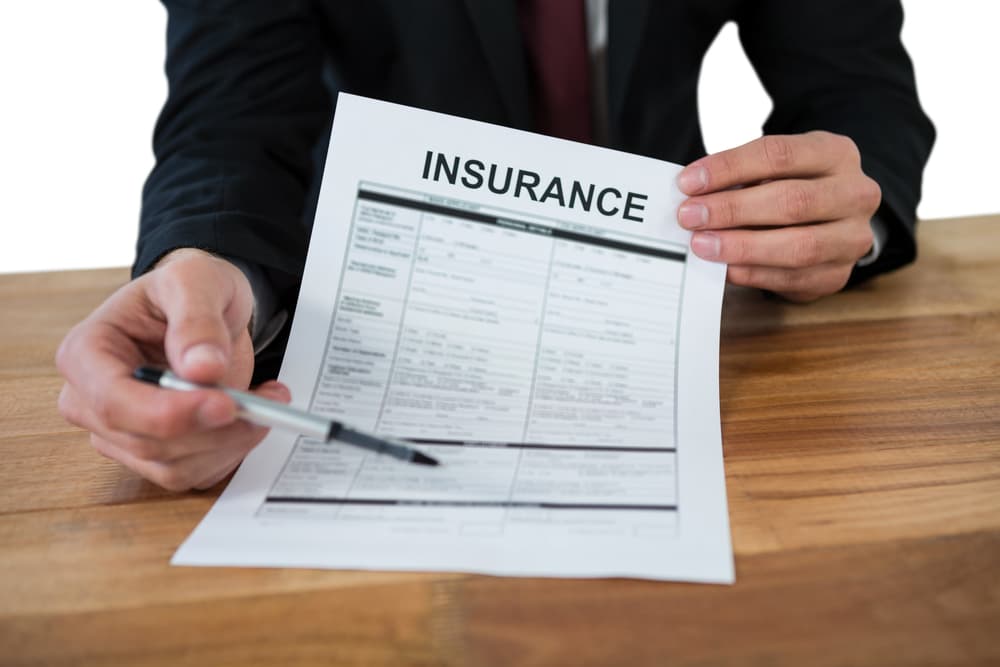 Midsection of a businessman seated at a desk, holding an insurance contract against a white background.