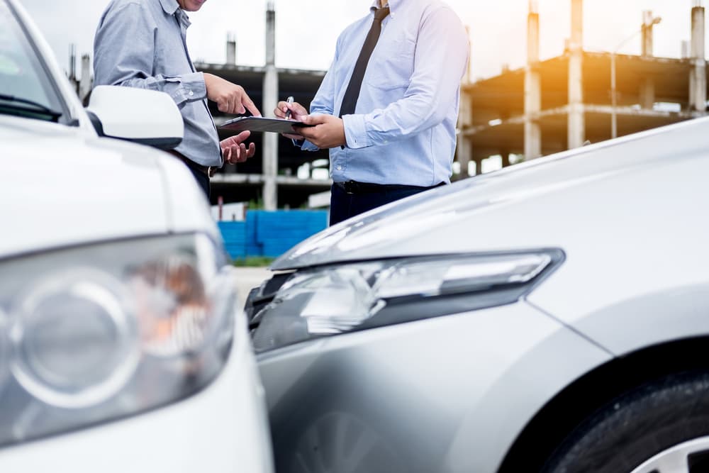An insurance agent writes on a clipboard while inspecting a car, assessing and processing an accident claim.