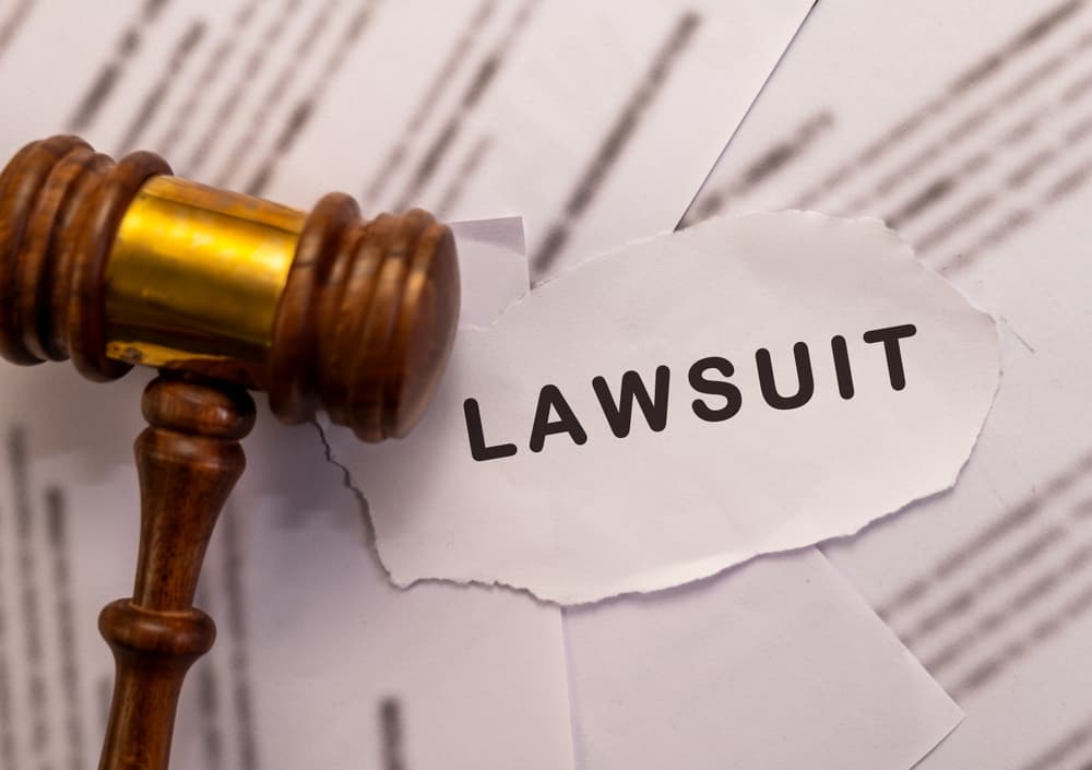 Wooden gavel beside torn paper with the word 'Lawsuit'—symbolizing legal action, court cases, and disputes.