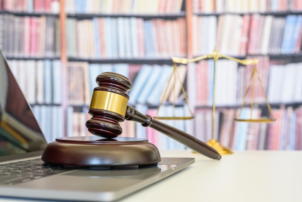 Legal office and justice concept: A judge's gavel and base rest on a desk in a courtroom, with the blurred scales of justice in the background.