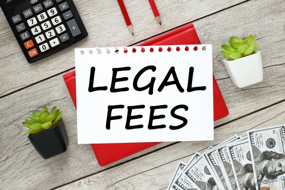 ‘Legal Fees’ text written on a red notepad placed on a wooden background.