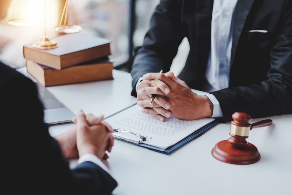 A male client sits at a wooden table in an office with a male lawyer, symbolizing legal advice and justice.