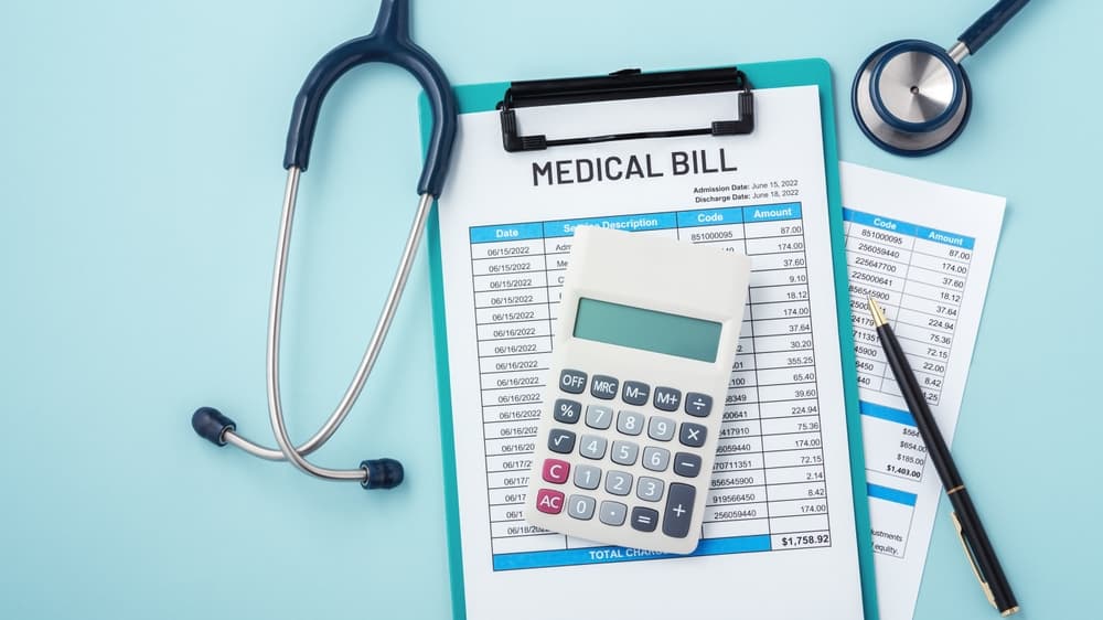 A calculator rests on a medical bill alongside a stethoscope and pen, set against a blue background with copy space, symbolizing healthcare expenses and financial planning.








