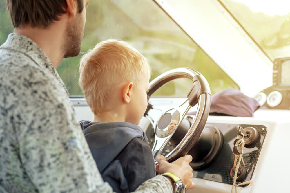 A father and son sit together behind the wheel of a boat, sharing a moment of bonding and navigation.