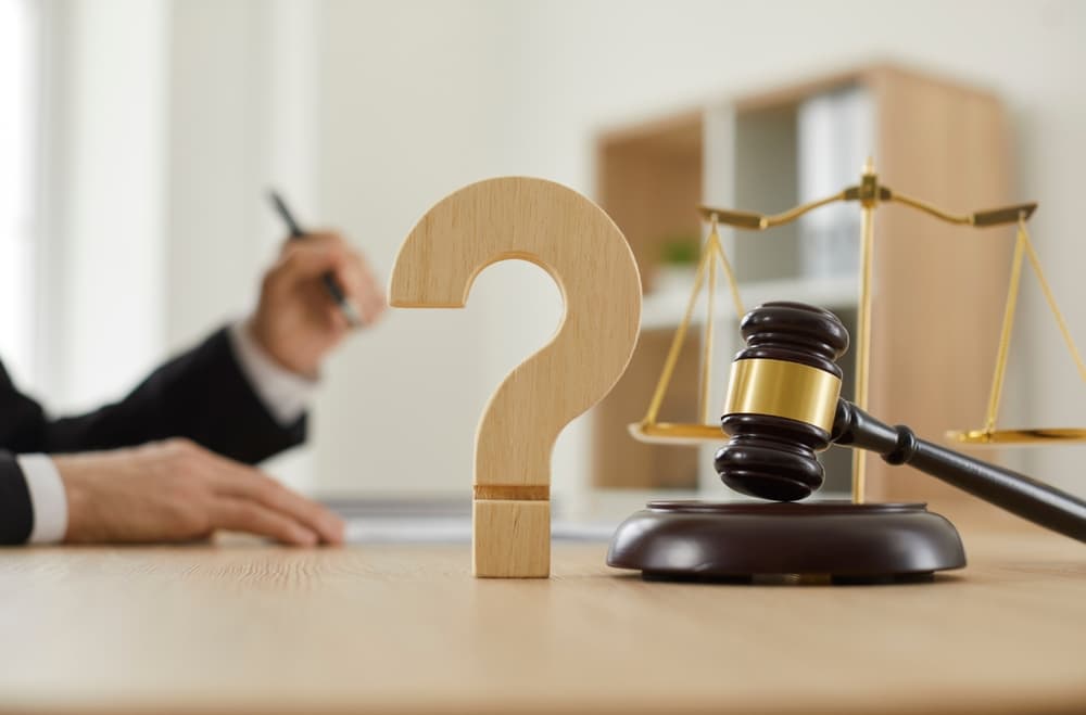 Close-up of a wooden question mark and gavel on a judge’s table or a lawyer’s desk, symbolizing law, justice, court trials, and professional legal services.