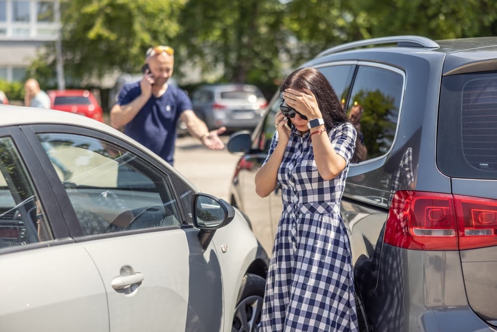 A frustrated woman talks on the phone after scratching a man's car, while the angry man calls the police in the background.
