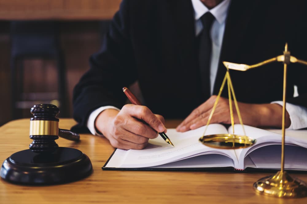A judge's gavel sits on the desk as a businessman or lawyer in a suit works on legal documents, symbolizing law, justice, and professional legal advice.