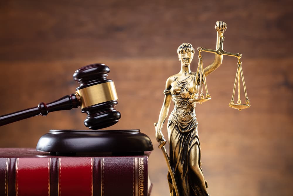 A close-up image features the golden Lady Justice statue beside a wooden gavel and a law book, symbolizing fairness, authority, and the foundation of legal principles.