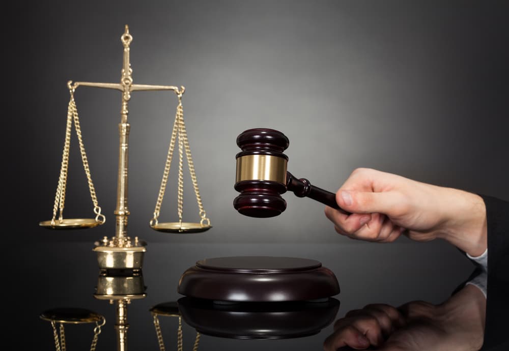 A cropped image shows a male judge holding a gavel with a justice scale on the desk, set against a black background, symbolizing authority, fairness, and the legal system.