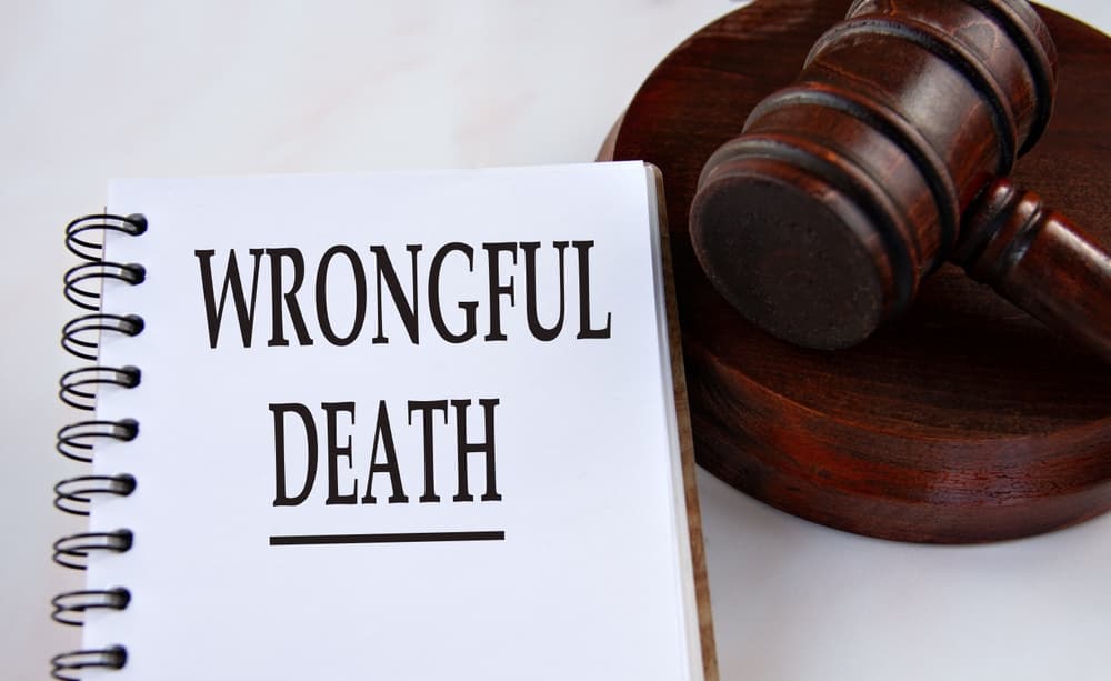 ‘WRONGFUL DEATH’ written in a white notebook, with a judge’s gavel in the background—symbolizing legal action and justice.