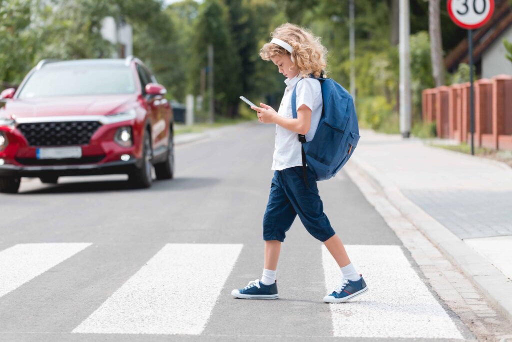Child distracted by smartphone while crossing crosswalk with approaching car, illustrating pedestrian safety risks. Child distracted by smartphone while crossing crosswalk with approaching car, illustrating pedestrian safety risks.