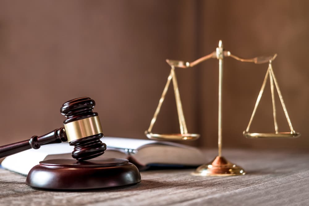 Scales of justice and a gavel rest on a wooden table beside a legal agreement, representing the concept of justice and law in a courtroom setting.
