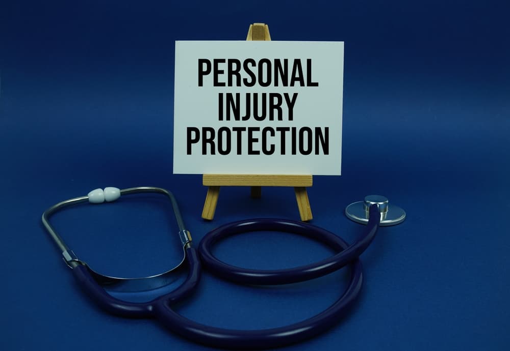 "Personal Injury Protection" text displayed on a paper card next to a stethoscope on a wooden surface.