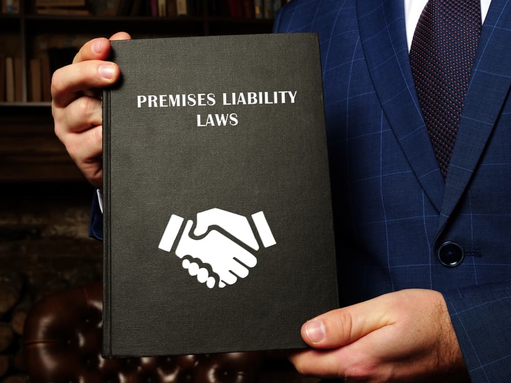 A lawyer holds a book titled PREMISES LIABILITY LAWS. A premises liability lawsuit holds a property owner accountable for injuries occurring on their property.