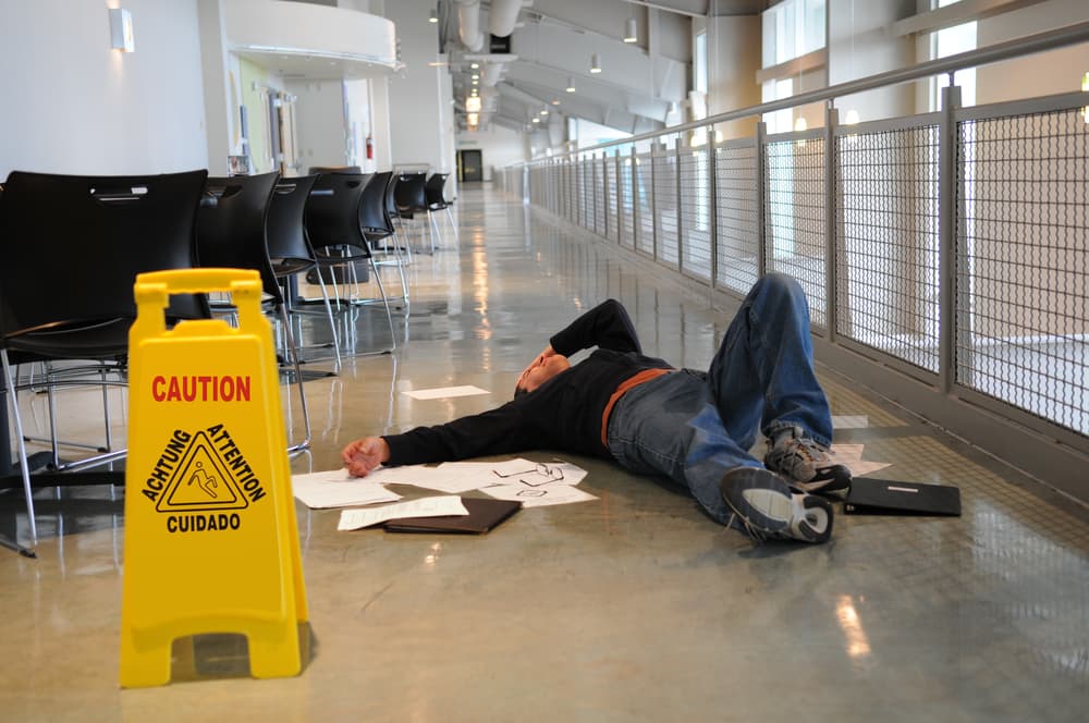 Man lying on a wet floor after slipping, despite a visible caution sign; selective focus on the man's head. Man lying on a wet floor after slipping, despite a visible caution sign; selective focus on the man's head.