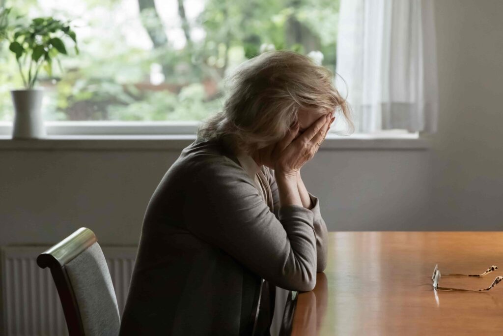 Sad woman sitting at table with head in hands feeling stressed and depressed at home.