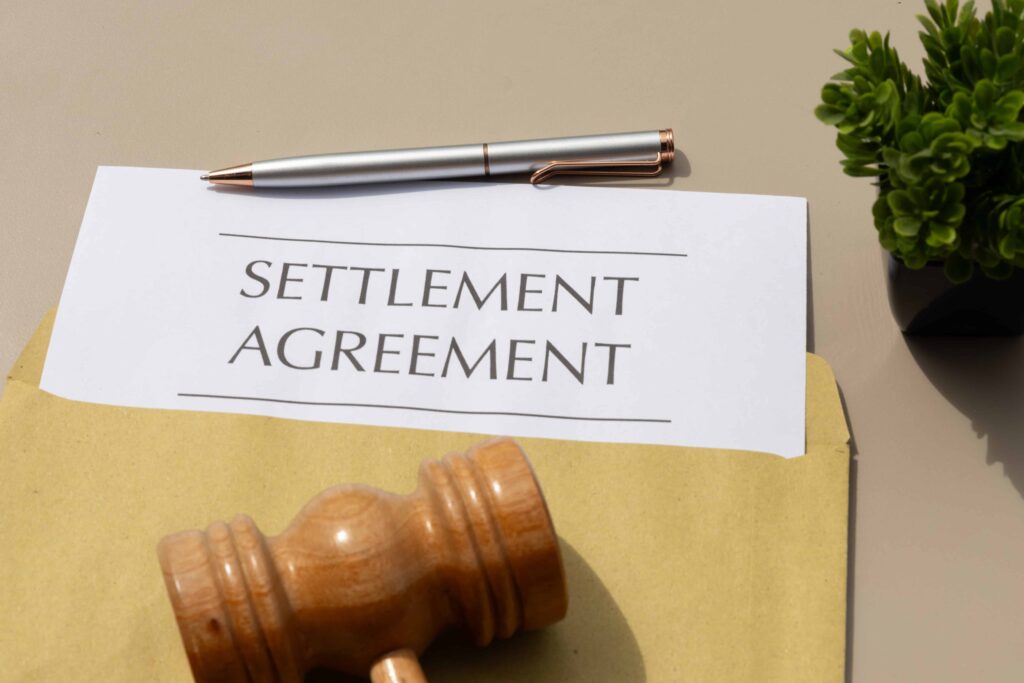 Settlement agreement document with judge’s gavel and pen on desk representing legal contract and case resolution.