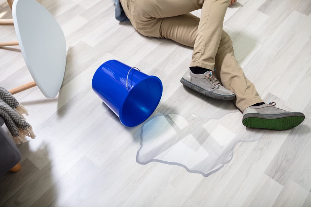 Mature man slipping on a wet floor beside a spilled bucket of water.