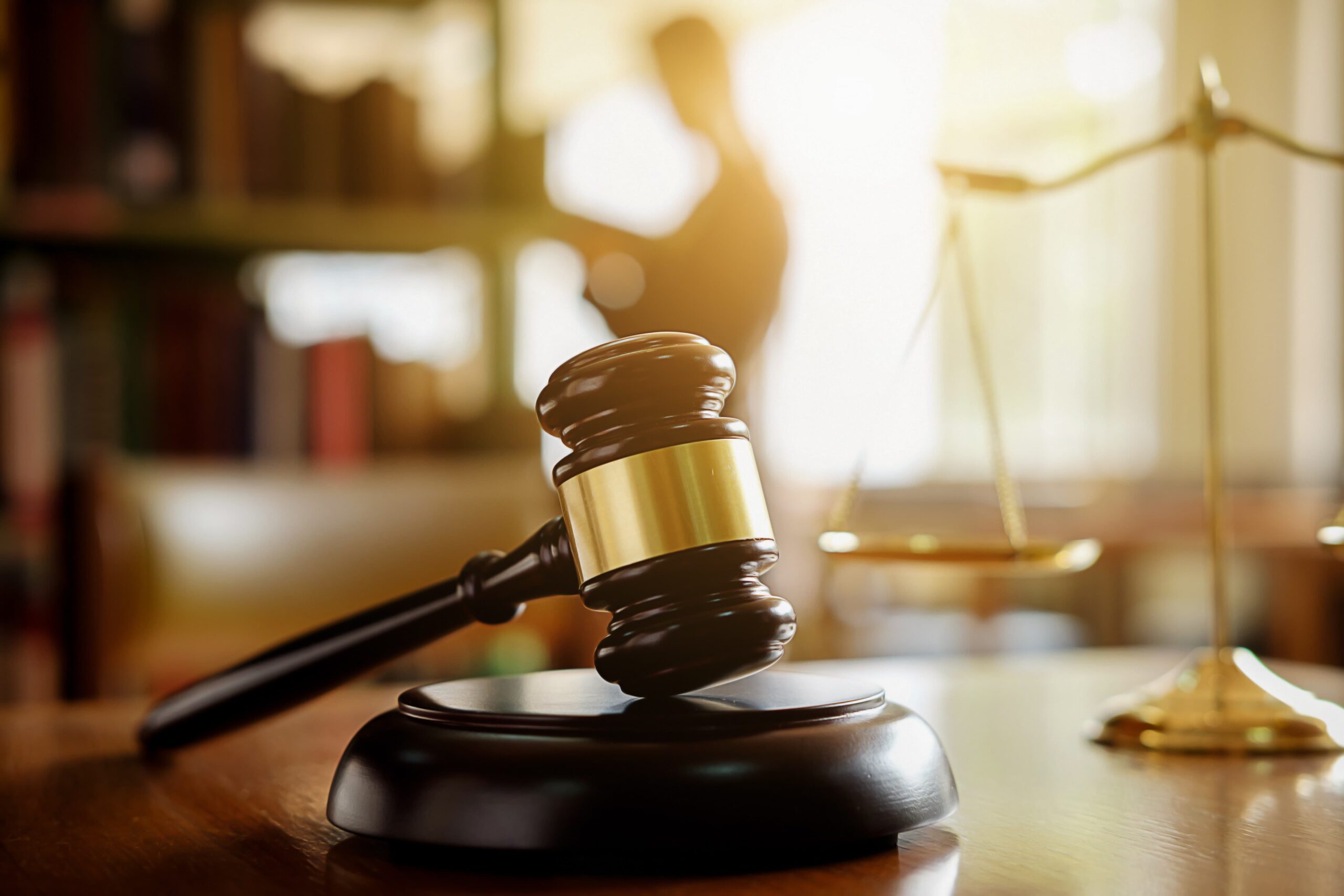 Judge’s gavel and golden scales of justice in courtroom symbolizing law, legal decisions, and justice system.