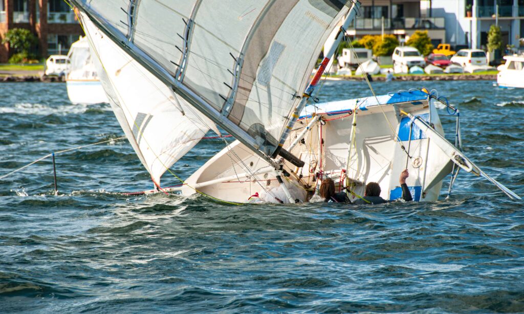 Capsized sailboat with people in the water after boating accident.