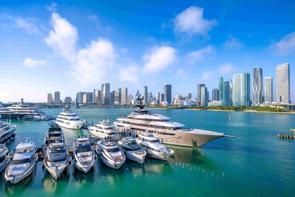 Luxury yachts docked at a marina with city skyline in the background on a sunny day.
