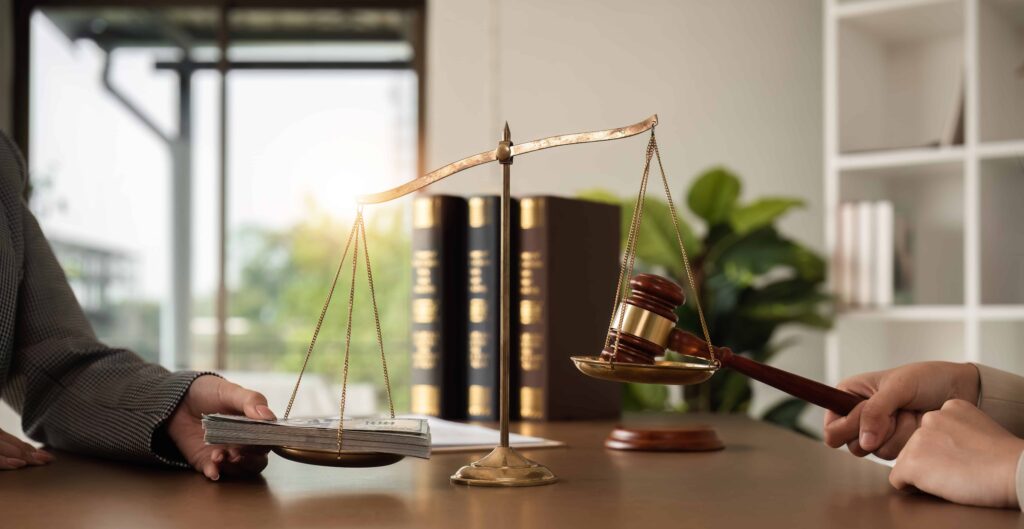 Scales of justice with gavel and money symbolizing legal settlement, bribery, or financial compensation in a law office.
