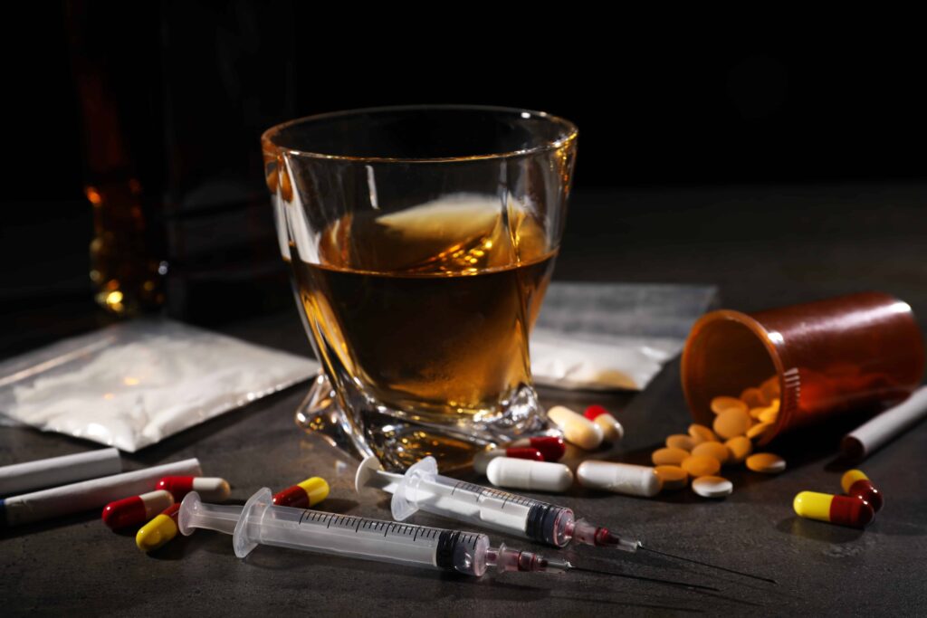 Alcohol, pills, syringes, and drugs on table symbolizing substance abuse and addiction risk.