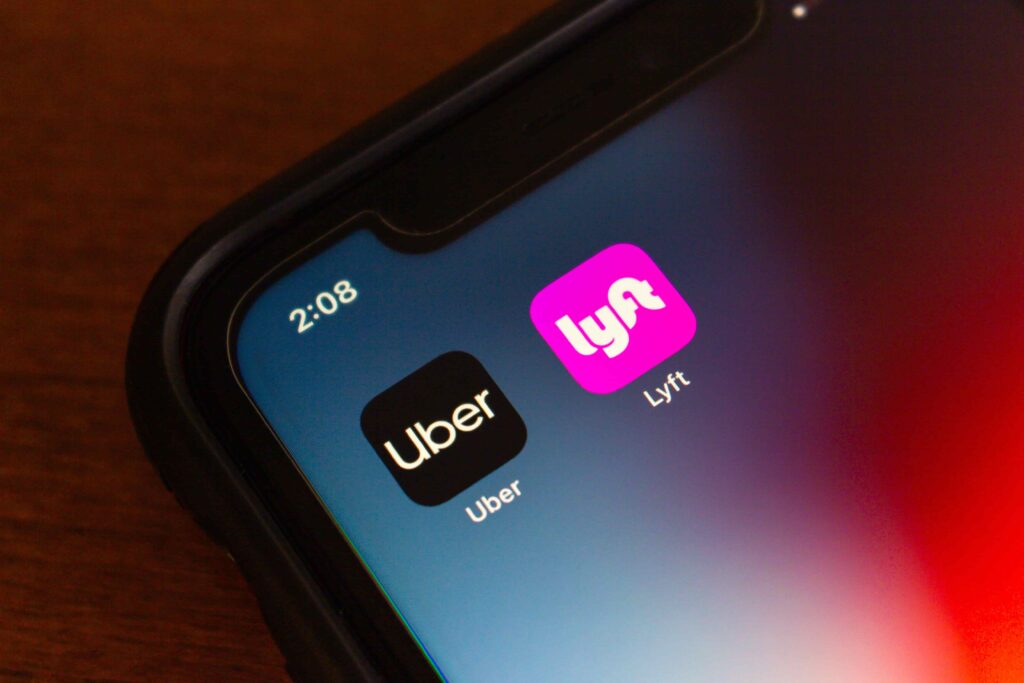 Close-up of a smartphone screen showing Uber and Lyft ride-sharing app icons. Close-up of a smartphone screen showing Uber and Lyft ride-sharing app icons.