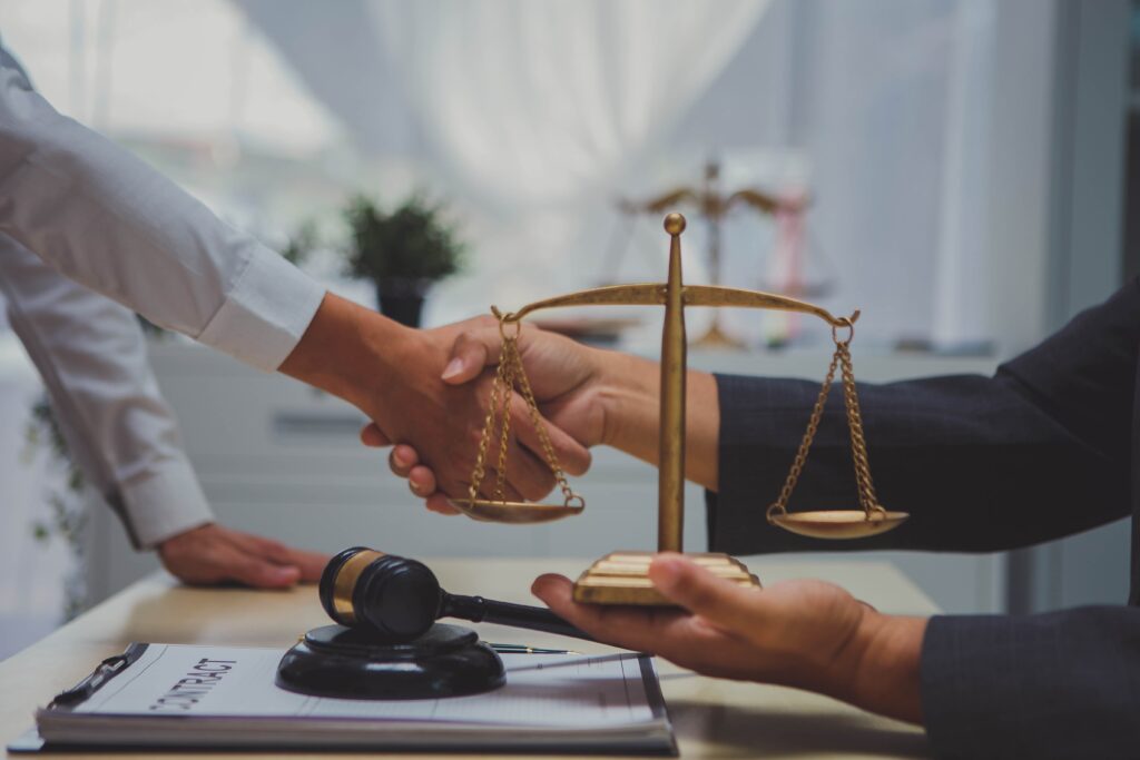 Lawyer and client shaking hands with justice scales and gavel on desk after successful legal agreement. Lawyer and client shaking hands with justice scales and gavel on desk after successful legal agreement.