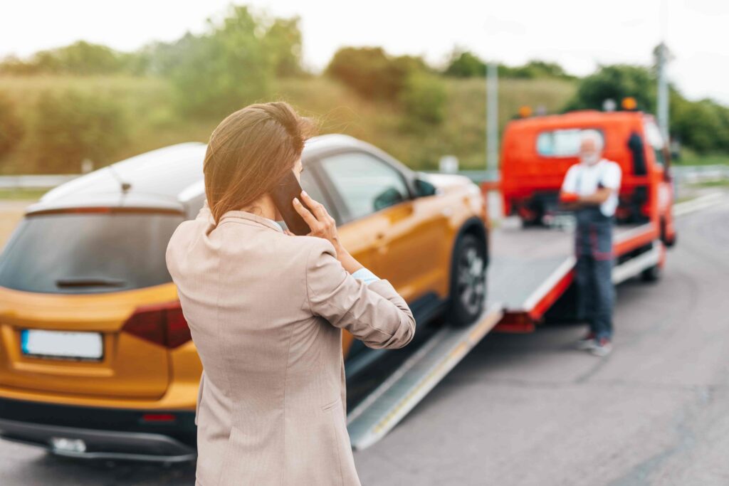 Woman calling for roadside assistance while her car is being towed after a breakdown.