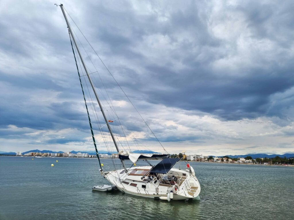 Sailboat anchored near the coast under cloudy skies with a city skyline in the background. Sailboat anchored near the coast under cloudy skies with a city skyline in the background.