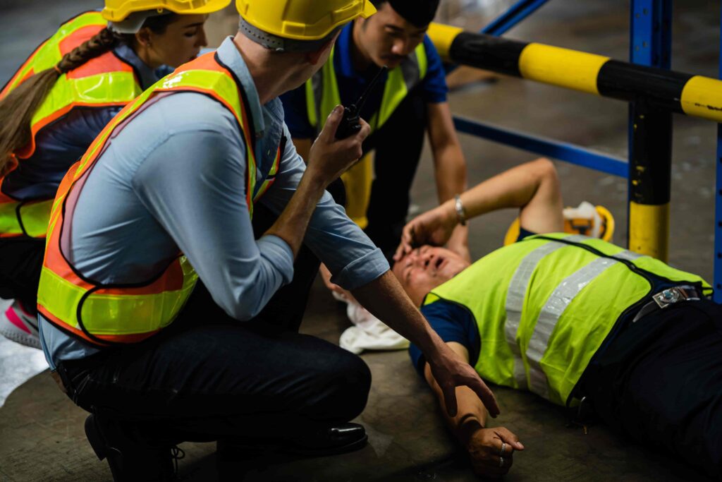 Construction workers assisting injured coworker after workplace accident in warehouse. Construction workers assisting injured coworker after workplace accident in warehouse.