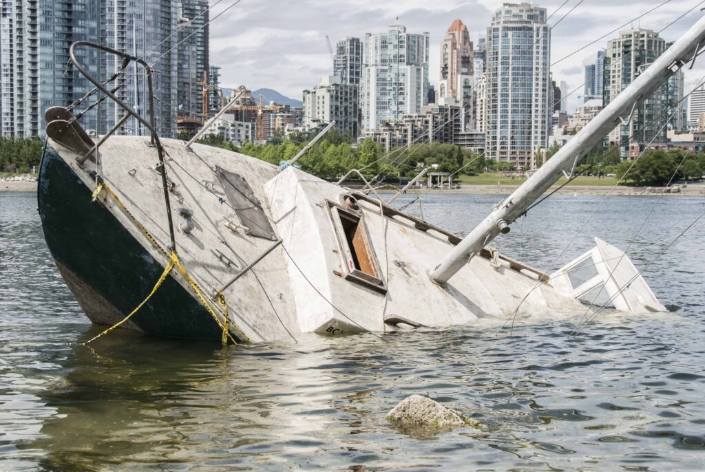 Partially sunken sailboat near city waterfront with modern skyscrapers in the background. Partially sunken sailboat near city waterfront with modern skyscrapers in the background.