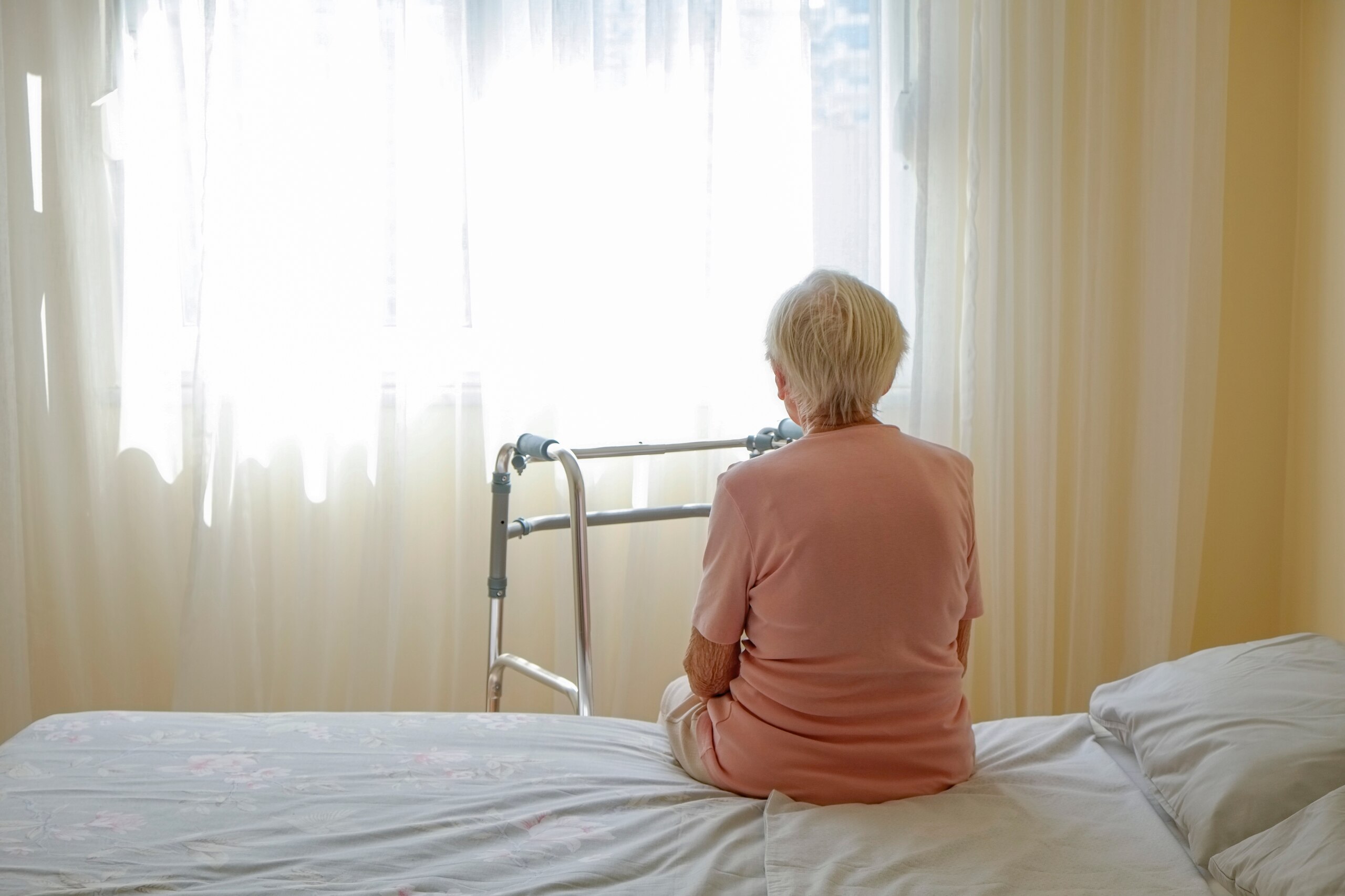 Senior sitting alone on a bed with a walker nearby, representing signs of emotional neglect in Florida nursing homes.