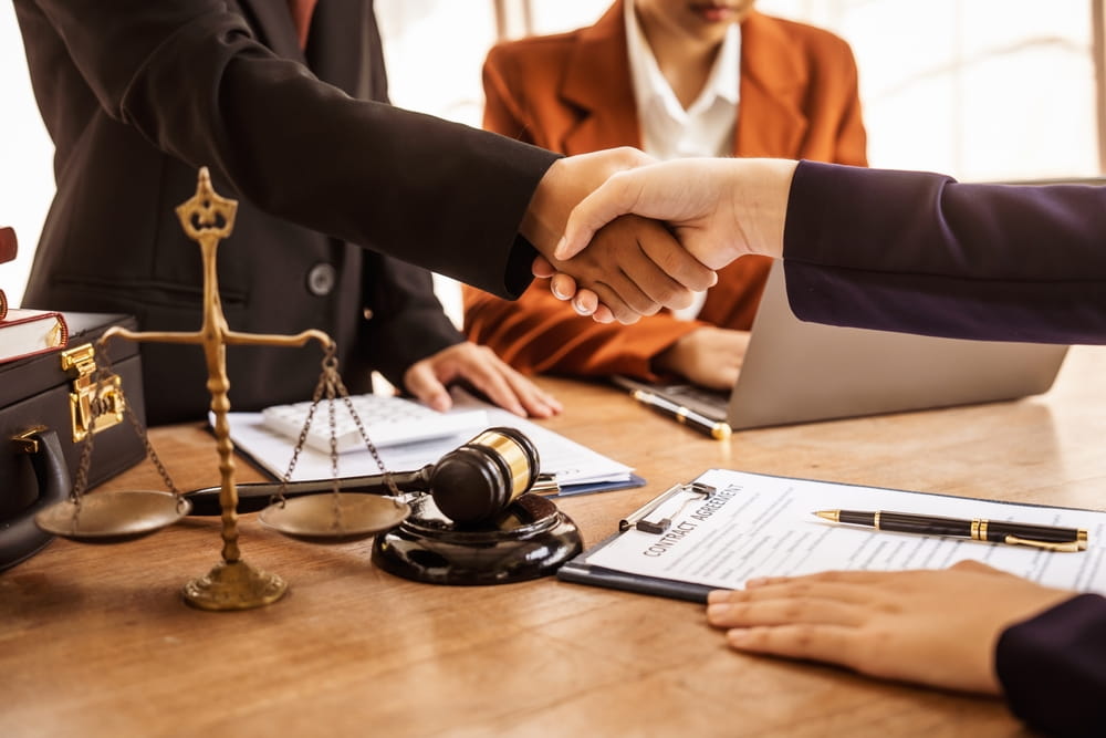 Two Boca Raton, FL motorbike accident attorneys shaking hands over a desk, symbolizing a successful client agreement.